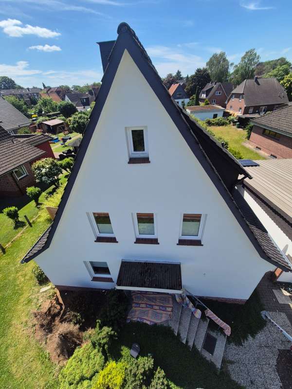 Weiß gestrichenes Giebelhaus mit dunklem Dach, fotografiert aus der Vogelperspektive vor blauem Himmel